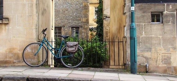 A blue bicycle standing by a metal fence between two houses