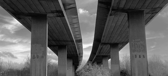 The view from below of two motorway bridges parallel to each other and a cloudy sky.