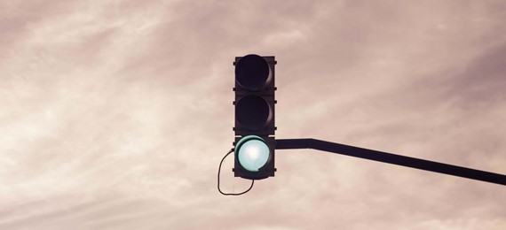 Green light of a street light with tree tops and pink sunset sky in the background.