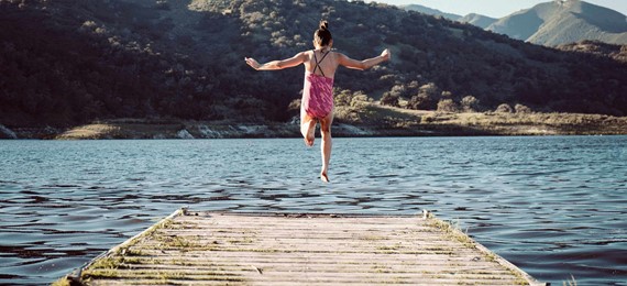 Girl leaping into a lake from a wooden platform.
