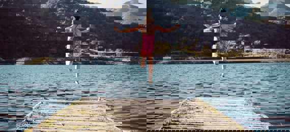 Girl leaping into a lake from a wooden platform.