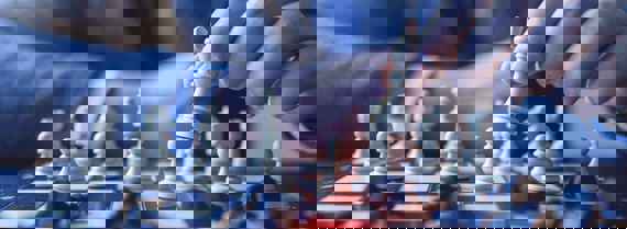 A chess board with a hand of a person holding one of chess pieces.