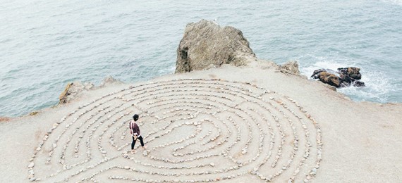 A person walking in a labyrinth made out of stones laid out on a beach.