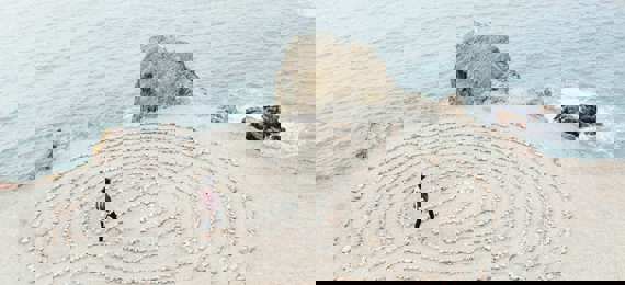 A person walking in a labyrinth made out of stones laid out on a beach.