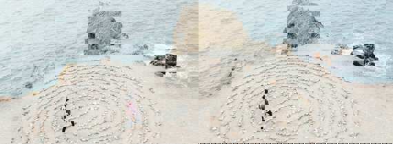 Image of person walking through a maze made of pebbles on a beach