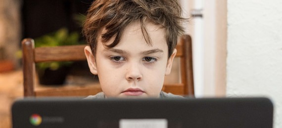 A child with messy hair looking at a laptop screen. His face has serious expression. 