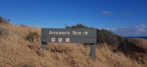 Grassy hillside with a sign showing an arrow pointing from left to right and words answers 1km There is an ocean slightly visible behind the hill.