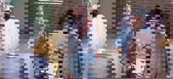 Group of people sitting in a circle. On person is talking and holding papers.