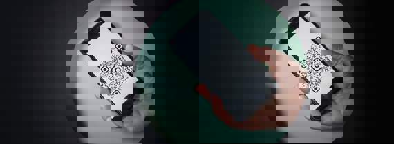 A hand holding cellphone. There is a QR code on the screen